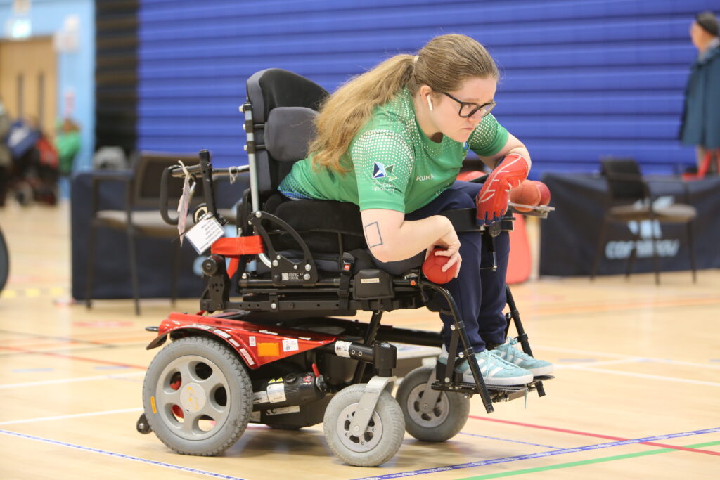 Claire is in her throwing position and ready to release the ball. She is wearing a green t shirt and her 1975 box tattoo is visible on her right arm