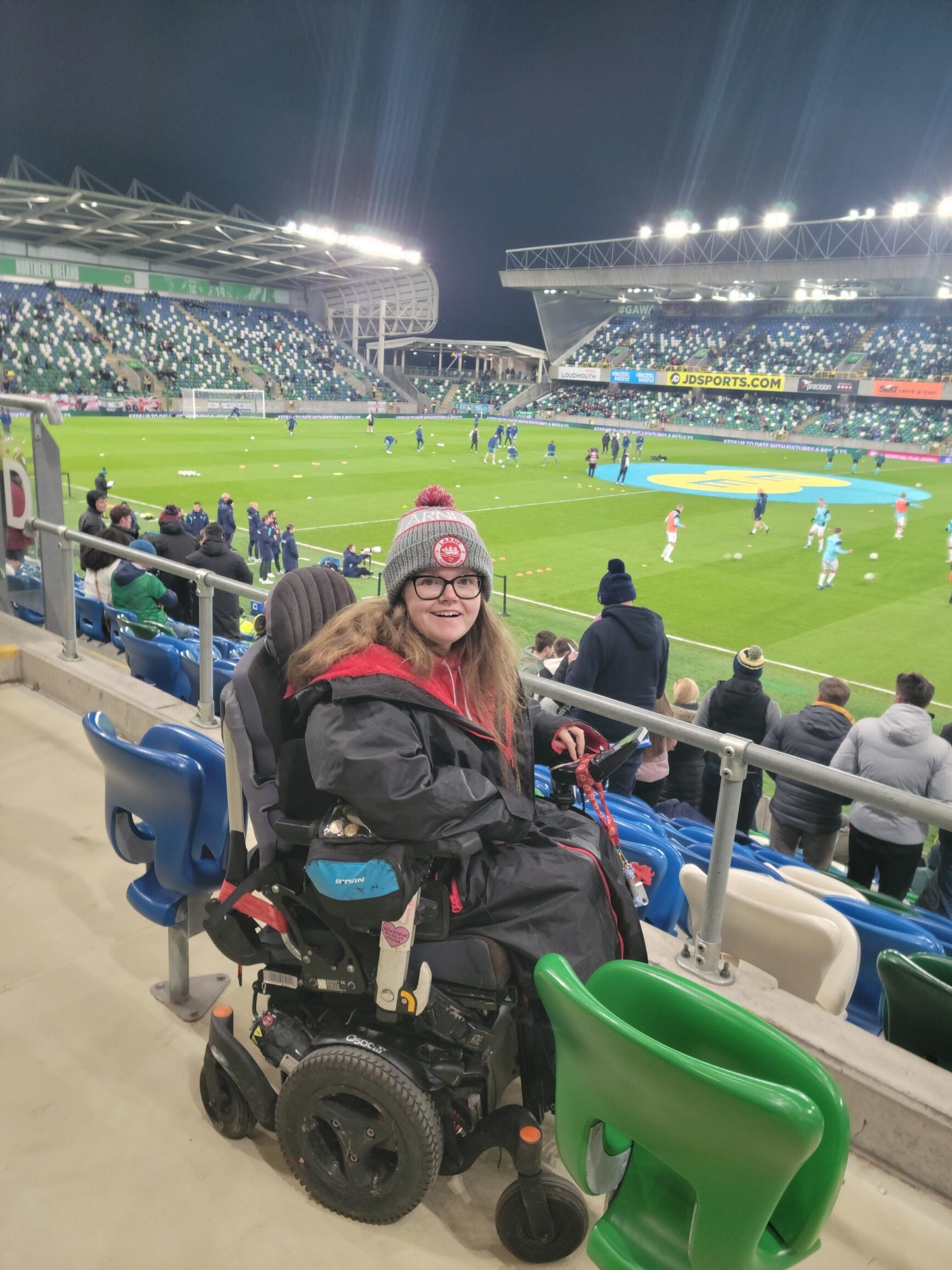 Claire is at the NI game vs Denmark. She is sitting in her powerchair at the side of the pitch.