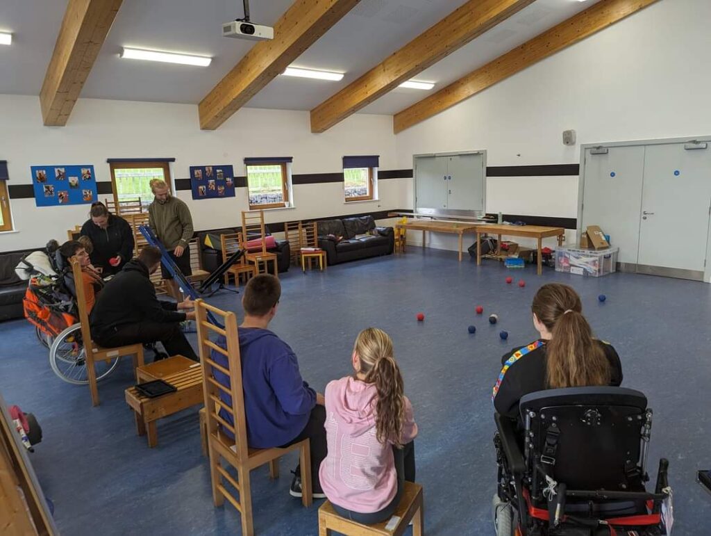 Claire is delivering a boccia session with the young adults all in a line on the left of the image